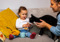 Child holding a tube of cat treat paste while a black-and-white cat sniffs towards it.