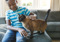 Child sitting on a sofa, stroking a brown cat standing beside them.